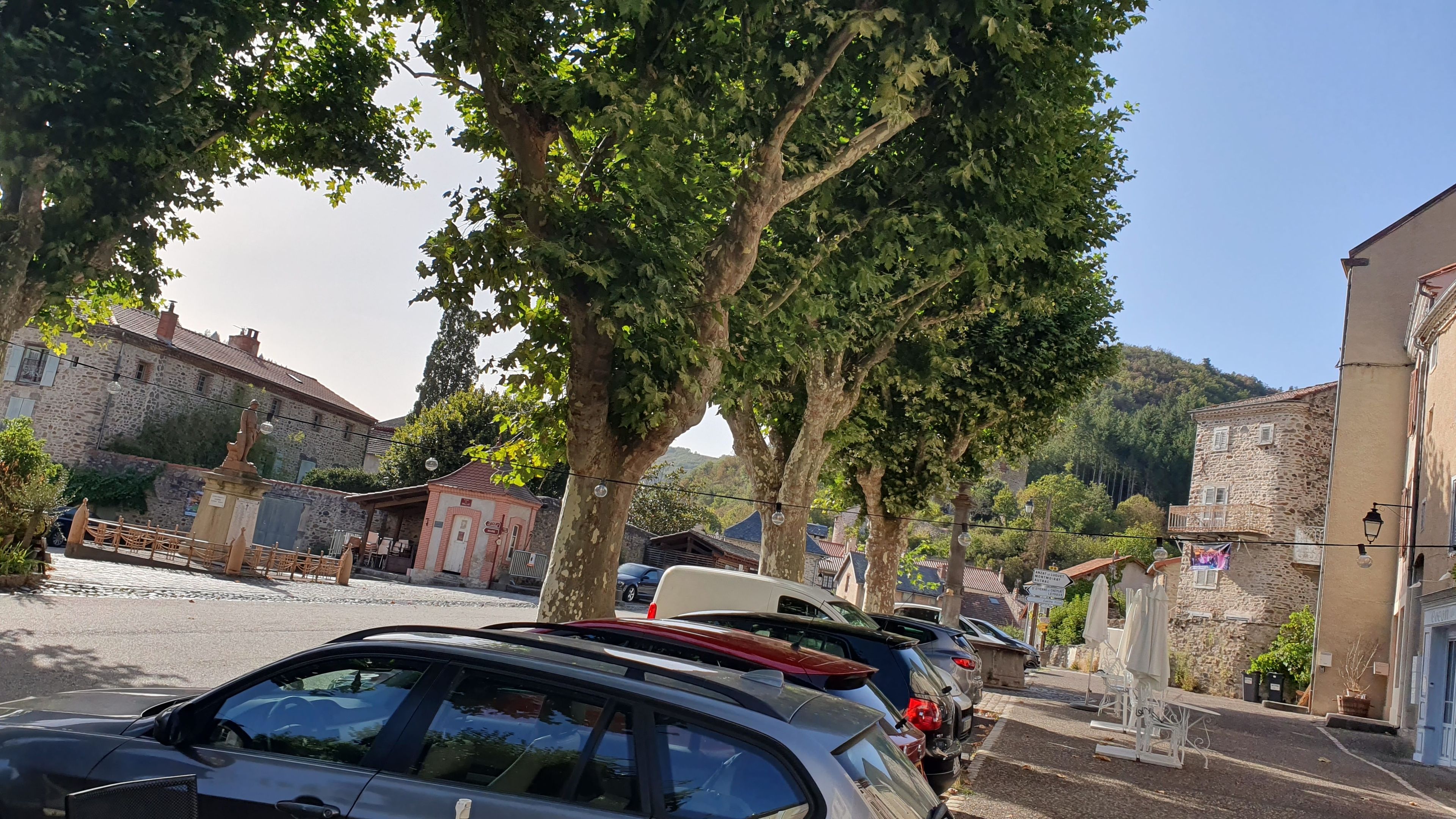 Une rue bordée de voitures garées, de bâtiments en pierre et d’arbres.