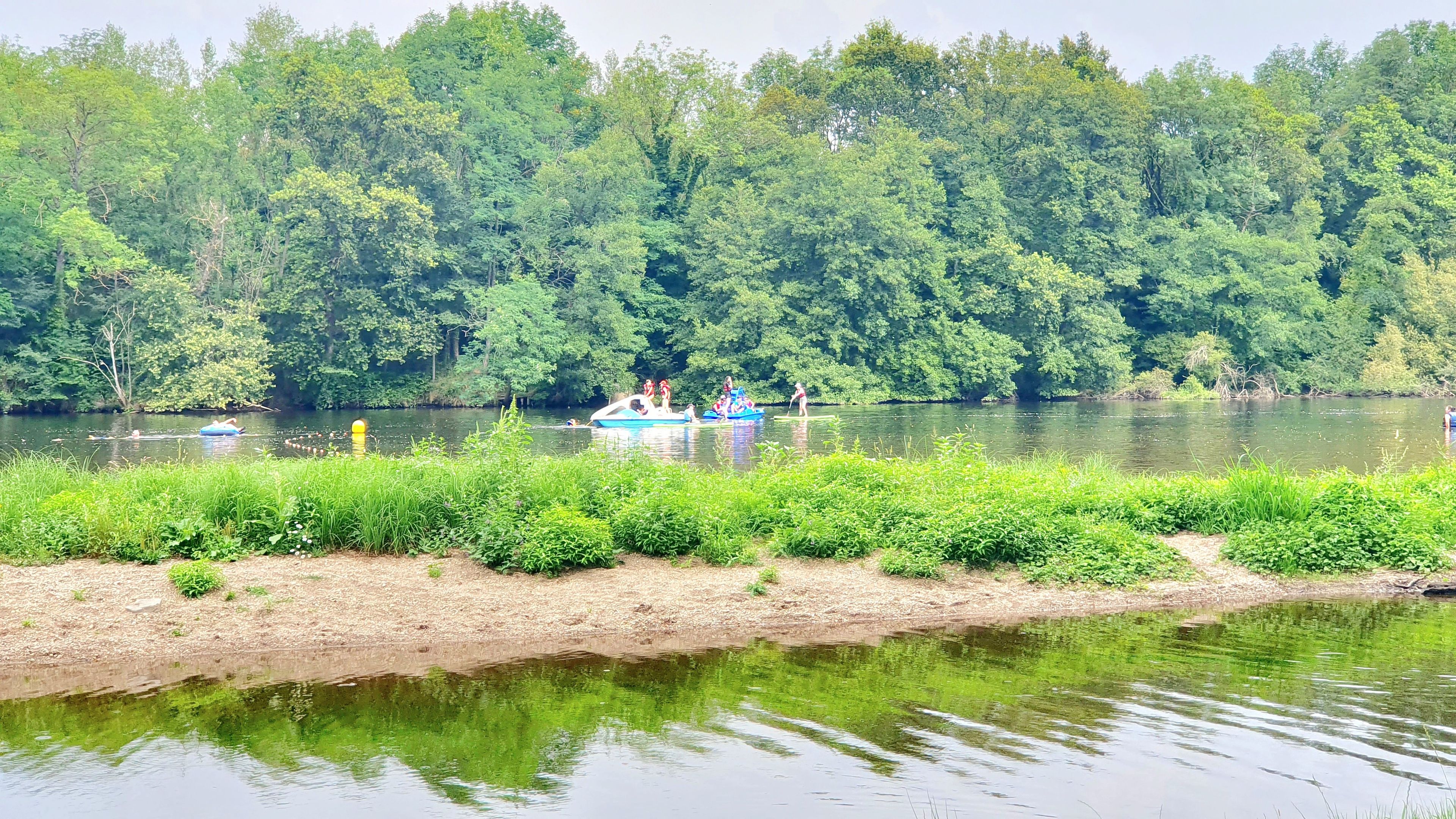 A river with boats and people, surrounded by dense greenery.