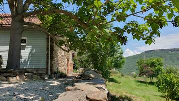 A rustic stone building with a sloped roof, surrounded by a gravel path and greenery.