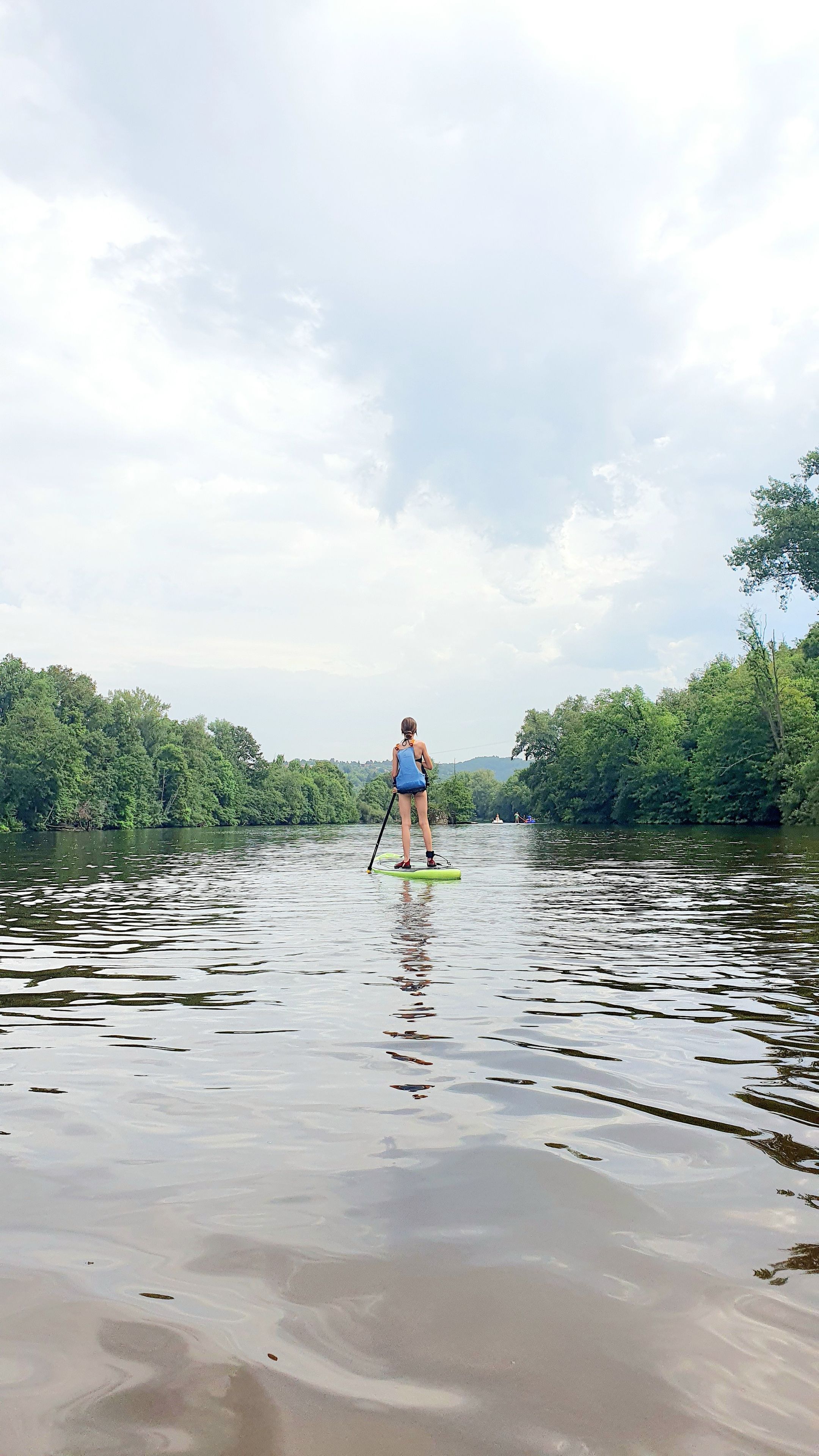 Une personne fait de la planche à rame sur une rivière paisible, entourée d’une végétation luxuriante.