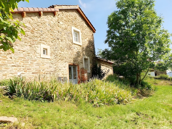 A stone building with a sloped roof, a door, and a window. - Holiday Home 'Le Poulailler' with Private Garden, Summer Kitchen and Stunning Views (Blesle)