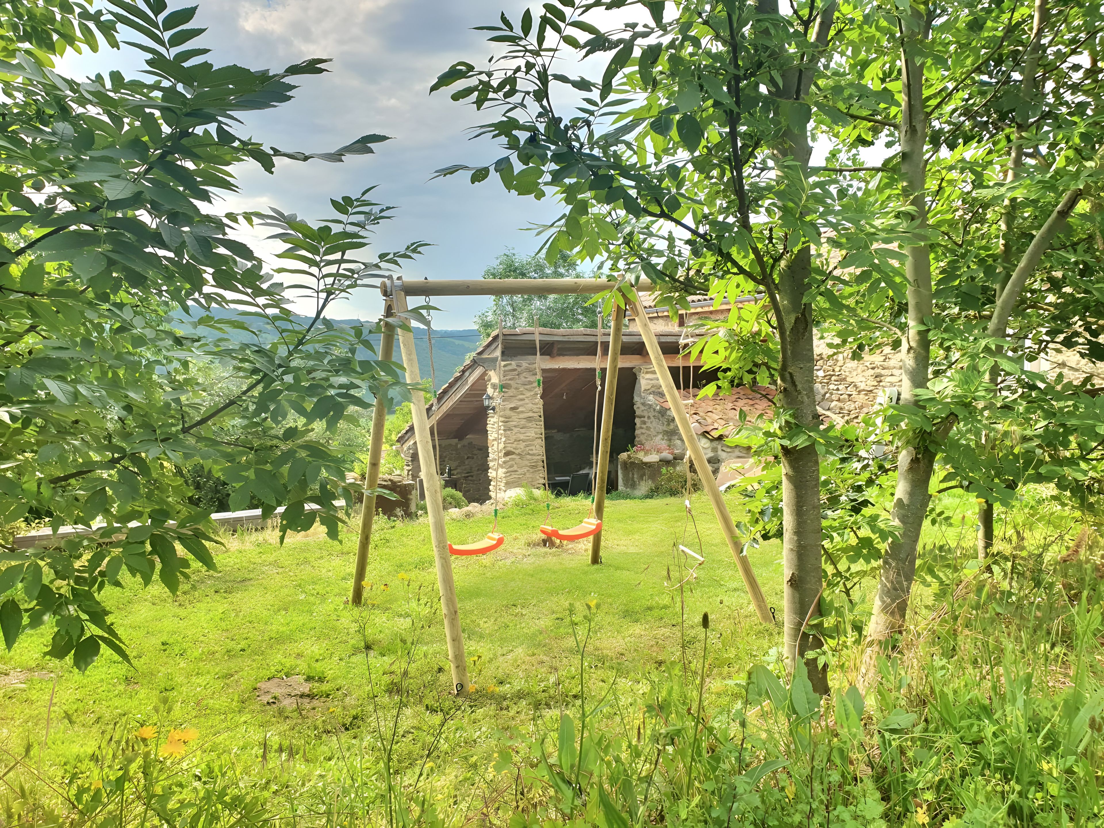 Un edificio rustico in pietra con un'altalena di legno in un rigoglioso giardino verde.