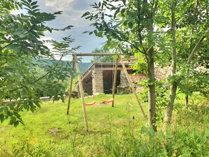 Een rustiek stenen gebouw met een houten schommel in een weelderige groene tuin.