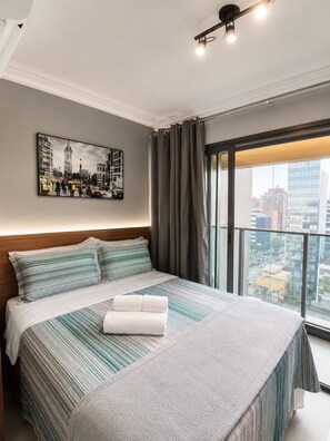 A hotel room with a large bed, a cityscape view, a framed picture on the wall, and a balcony with curtains. - On Paulista 815 (Vila Mariana)