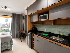 A compact kitchen with a microwave, sink, and a dining area with a table and chairs. - On Paulista 815 (Vila Mariana)