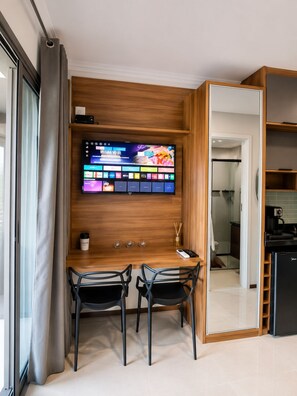 A modern room with a wooden wall-mounted TV, two chairs, a small table, and a mirror. - On Paulista 815 (Vila Mariana)