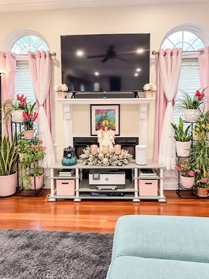 Una sala de estar con un televisor de pantalla plana sobre la chimenea, rodeada de plantas en macetas y un centro decorativo.