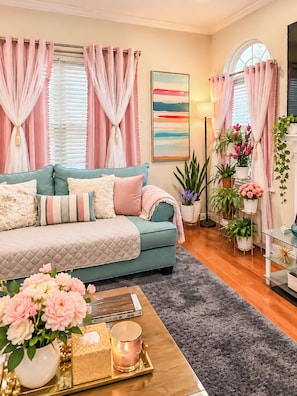 A cozy living room with a teal sofa, a coffee table with a candle, and a large window with curtains. - Mandale Ct - Two-Story Shared Home (Fort Washington)