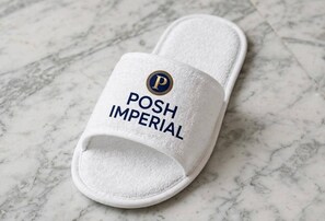 Una sandalia tipo chancla blanca con el texto 'POSH IMPERIAL' y un logotipo sobre una superficie de mármol.