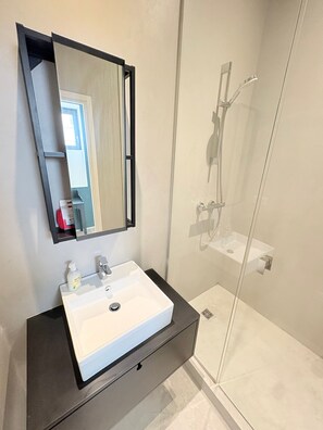Un bany modern amb un lavabo blanc, un mirall i una dutxa amb envàs de vidre.