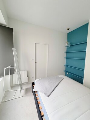 Un dormitori amb llit, un radiador blanc, una porta i un moble blau a la paret.