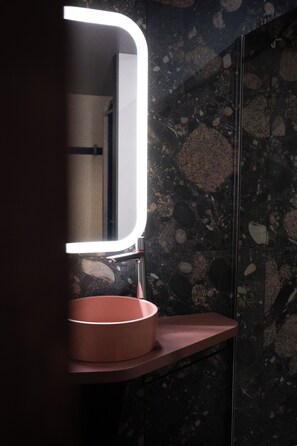 A bathroom with a round sink, a mirror with a light, and a dark speckled wall. - Oceania Paris 17 (Paris)