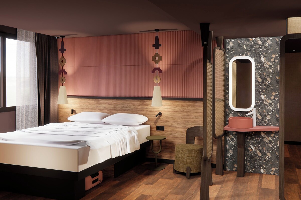 A modern hotel room with a wooden bed, a round mirror, a small round table, and a seating area.
