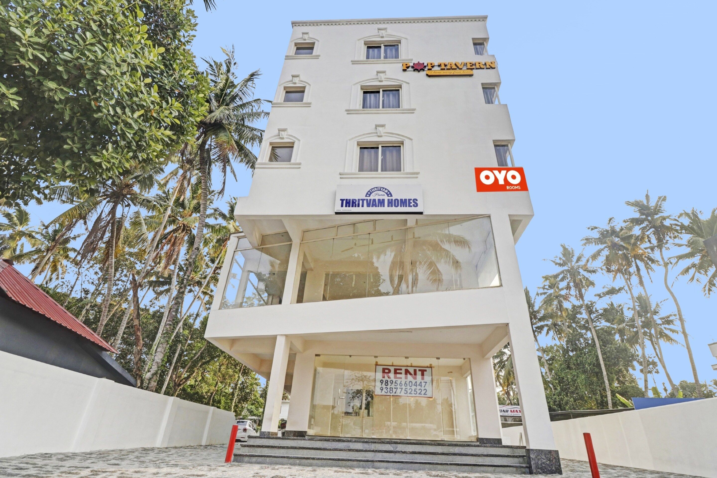 Un edificio de varios pisos con un letrero 'THRITVAM HOMES', un letrero que dice 'ALQUILER' y un letrero 'OYO ROOMS'.