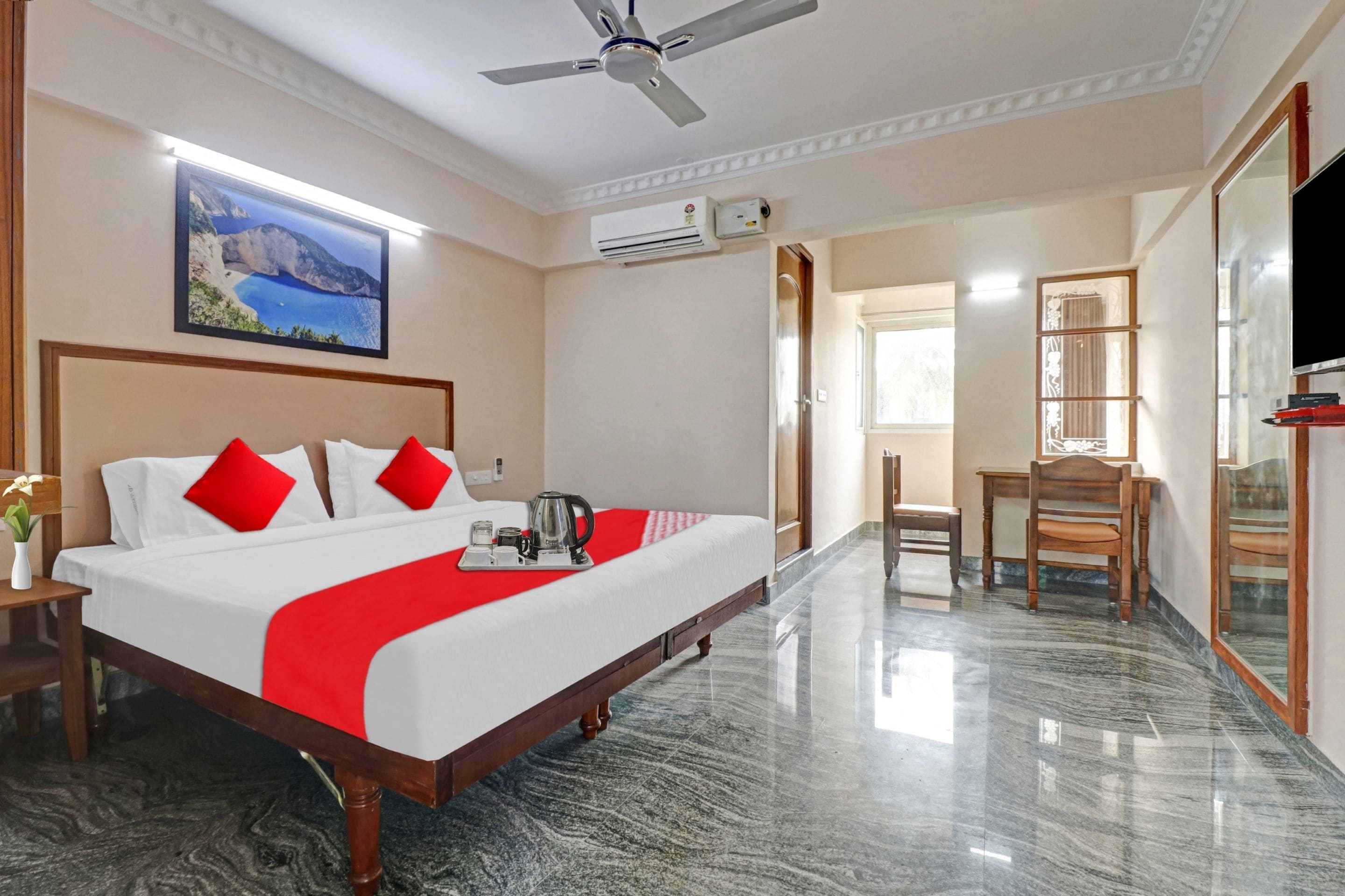 A hotel room with a bed, a desk, a chair, a television, and a painting on the wall.