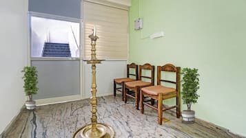 Una stanza con pavimento in marmo, una lampada a olio in ottone, due piante in vaso e tre sedie di legno.