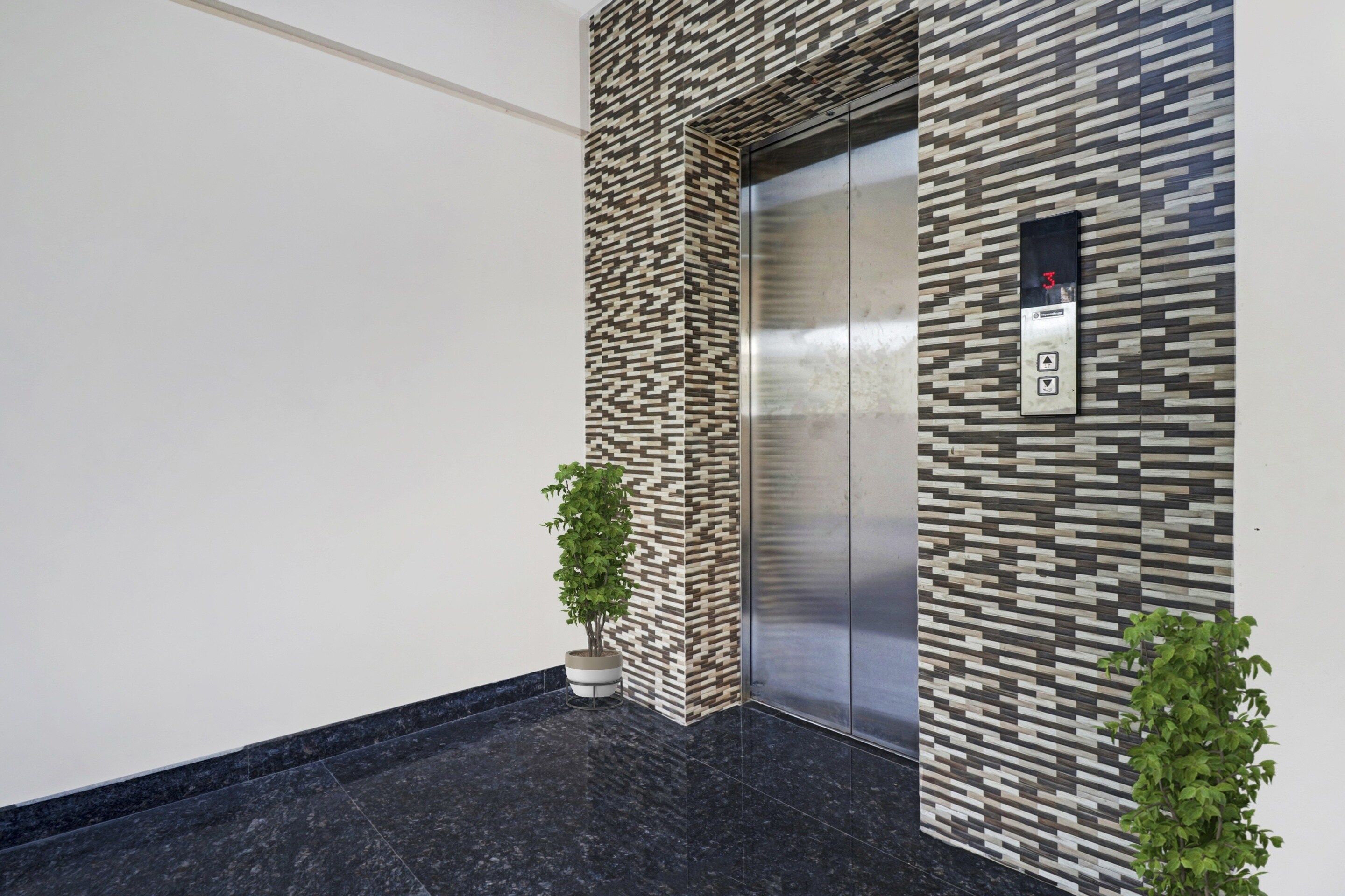 Un ascensor con un revestimiento de pared con diseño, una pantalla digital y dos plantas en macetas.
