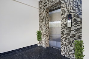 Un ascensor con un revestimiento de pared con diseño, una pantalla digital y dos plantas en macetas.