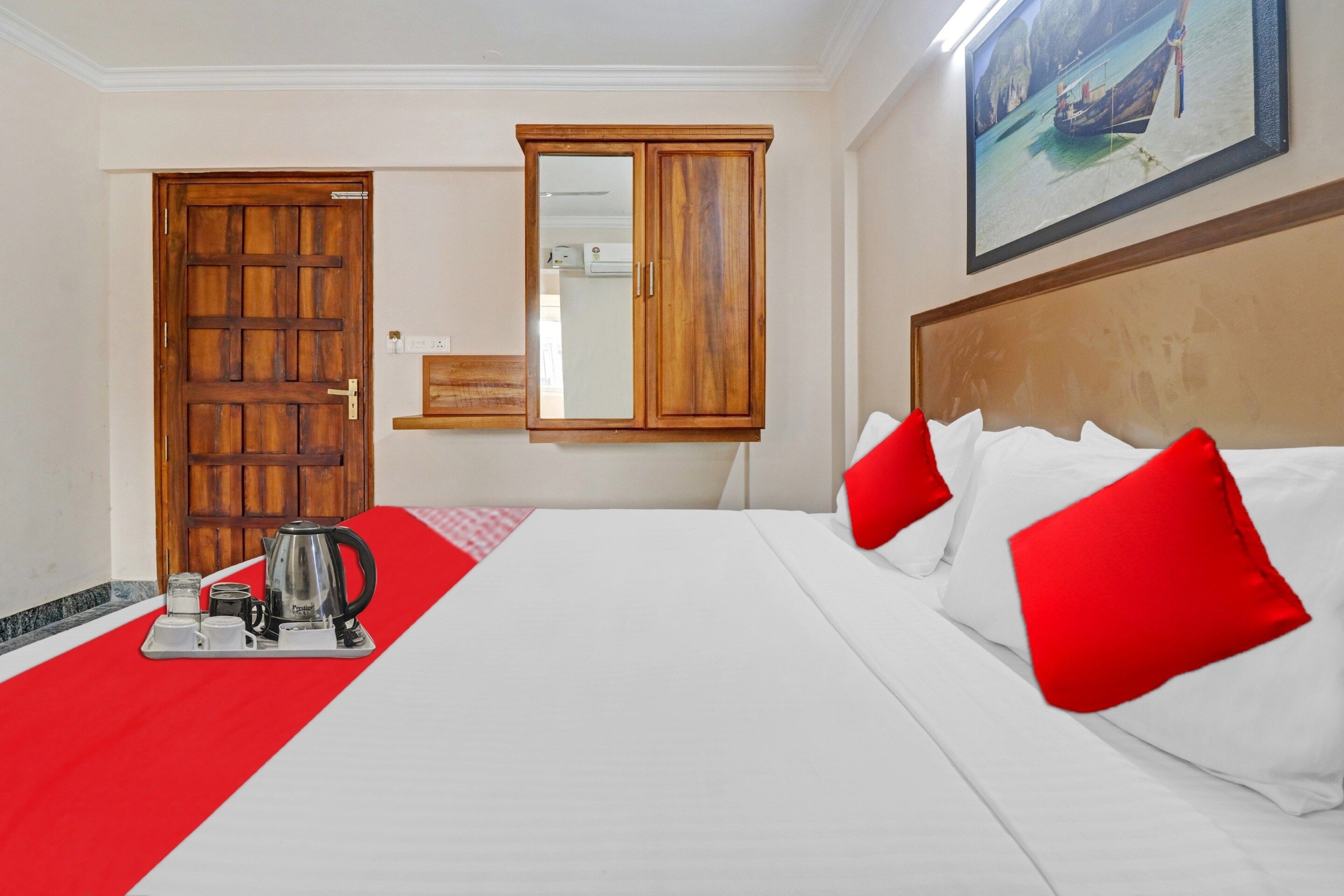 Habitación de hotel con cama, cafetera, bandeja con tazas, puerta de madera y un cuadro en la pared.