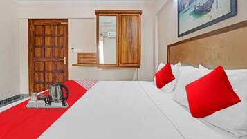 Habitación de hotel con cama, cafetera, bandeja con tazas, puerta de madera y un cuadro en la pared.