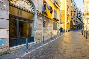 A narrow cobblestone street with historic buildings, a shop with a large window, and a sign reading "NAPOLI". - Montesanto Flow Flat by Napoliapartments (Naples)