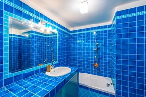 A bathroom with blue tiles, a white sink, a mirror, and a bathtub. - Montesanto Flow Flat by Napoliapartments (Naples)