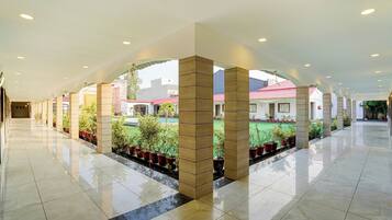 A spacious indoor area with a tiled floor, a central garden with potted plants, and a view of buildings outside.