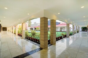 A spacious indoor area with a tiled floor, a central garden with potted plants, and a view of buildings outside. - Townhouse Oak Rapti Riverview Formerly (Gorakhpur)