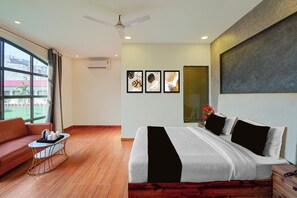 A hotel room with a bed, a sofa, a small table, and a window with a view of buildings. - Townhouse Oak Rapti Riverview Formerly (Gorakhpur)