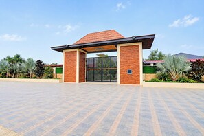 A modern building entrance with a brick facade, a metal gate, and a paved area with palm trees. - Townhouse Oak Rapti Riverview Formerly (Gorakhpur)