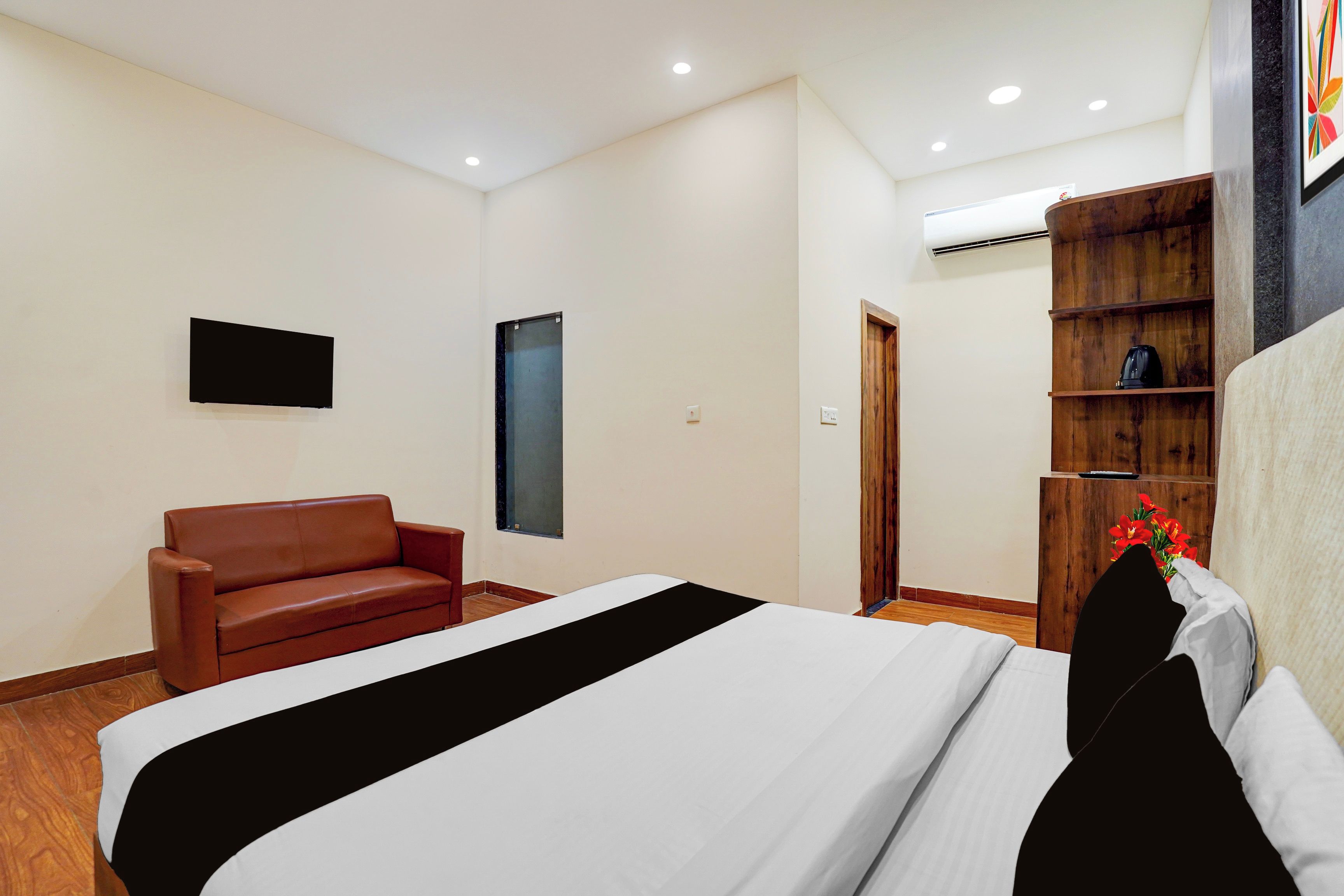 Habitación de hotel con cama, sofá de cuero marrón, repisa de madera con cafetera y televisor montado en la pared.