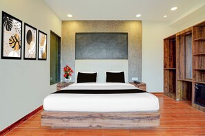 A modern bedroom with a large bed, a stone accent wall, and a wooden bookshelf. - Townhouse Oak Rapti Riverview Formerly (Gorakhpur)