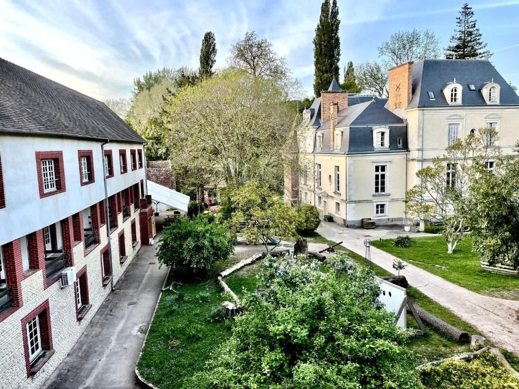 A courtyard with a building featuring a brick facade and multiple windows, surrounded by lush greenery and trees.