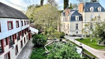 A courtyard with a building featuring a brick facade and multiple windows, surrounded by lush greenery and trees.