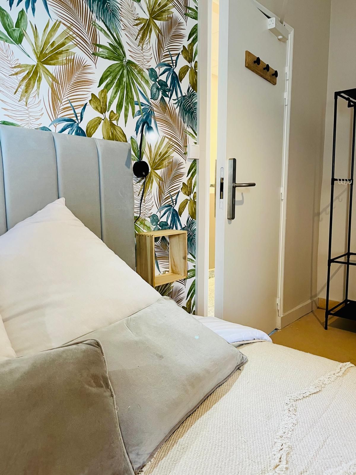 Un dormitorio con una cama, una puerta, un estante de madera pequeño y un soporte de metal negro.