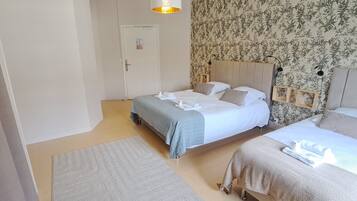 Ein Hotelzimmer mit zwei Betten, einem grauen Teppich, blumigem Wandpapier und einer Pendelleuchte.