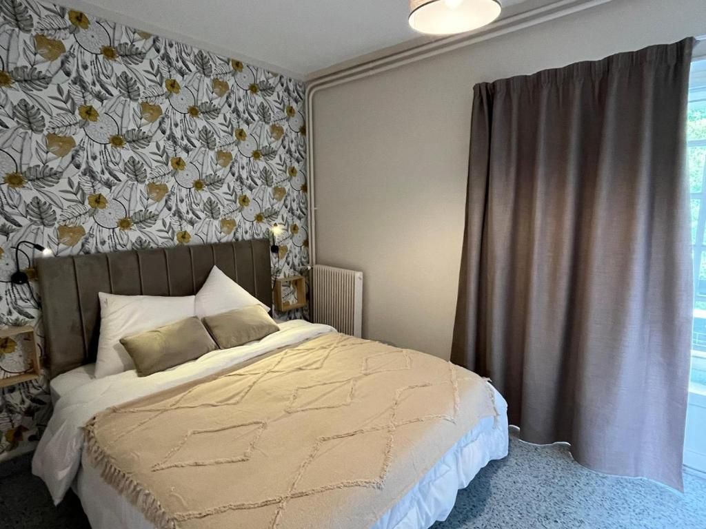 A hotel room with a bed, a radiator, and a window with curtains.