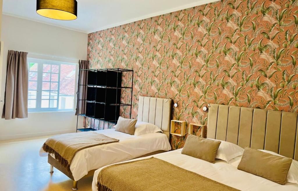 A hotel room with two beds, a large window, and a patterned wallpaper.