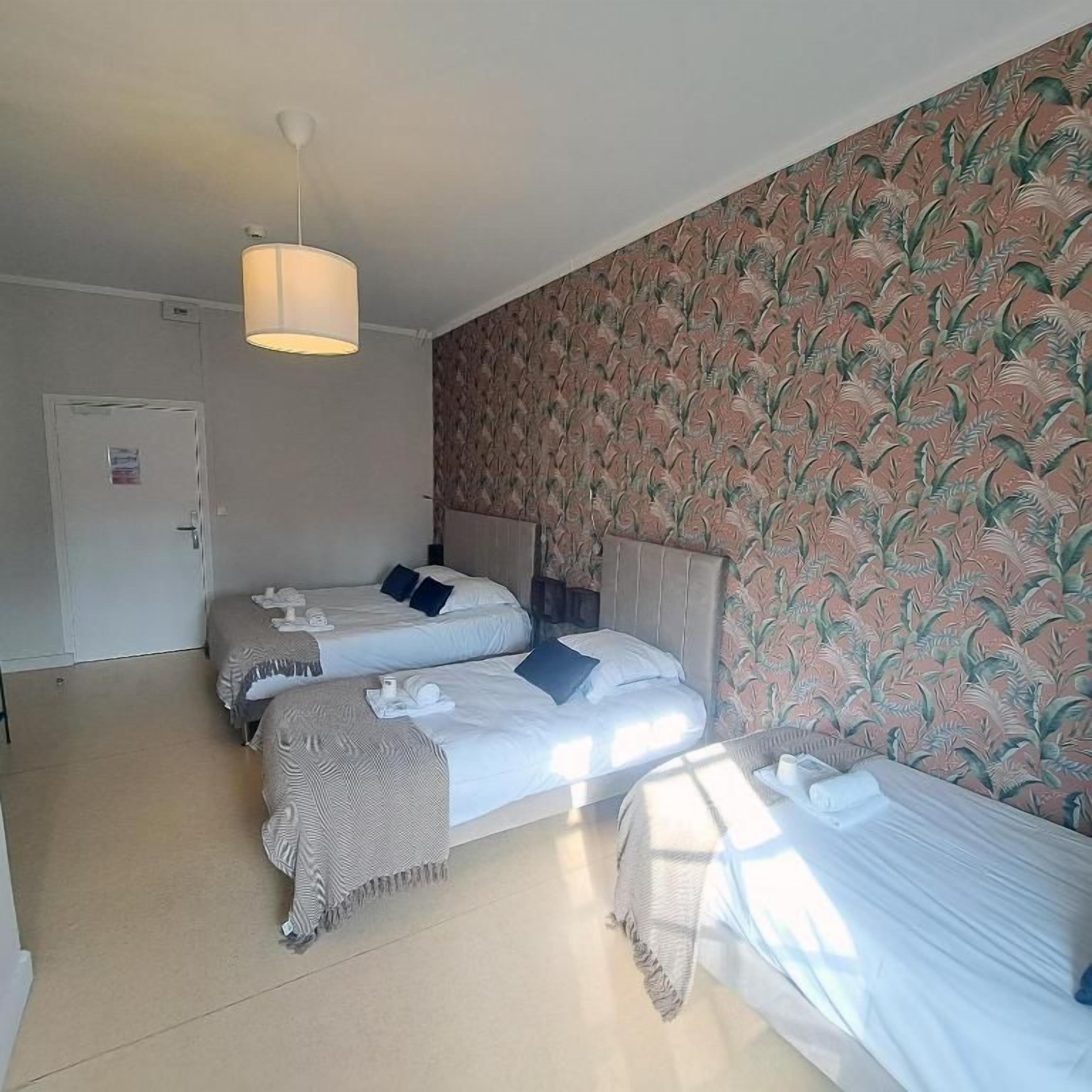 Habitación de hotel con dos camas, una puerta y un papel tapiz estampado.