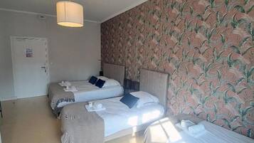 Habitación de hotel con dos camas, una puerta y un papel tapiz estampado.