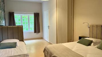 A hotel room with two beds, a window with curtains, a radiator, and a bedside table.