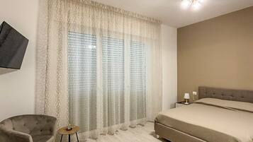 Een slaapkamer met een bed, een stoel, een klein tafeltje, een aan de muur bevestigde televisie en een plafondlamp.