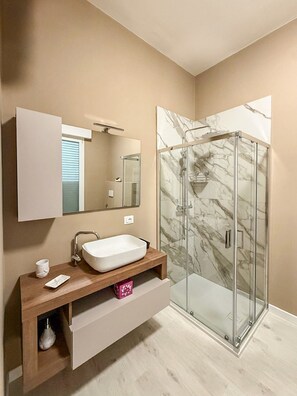 A modern bathroom with a glass shower enclosure, a white sink, and a vanity with storage. - defaultName (Termoli)
