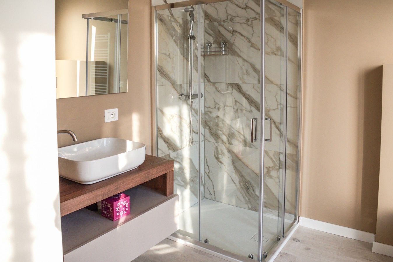 Une salle de bain moderne avec une douche à parois de verre, un lavabo sur colonne blanc et un meuble-lavabo en bois.
