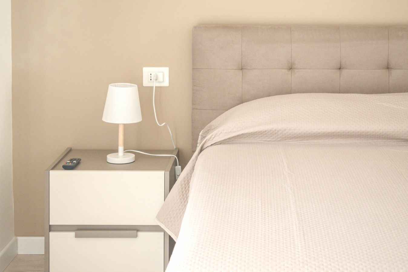 Ein Schlafzimmer mit einem Bett, einem Nachttisch, einer Lampe und einer Fernbedienung.