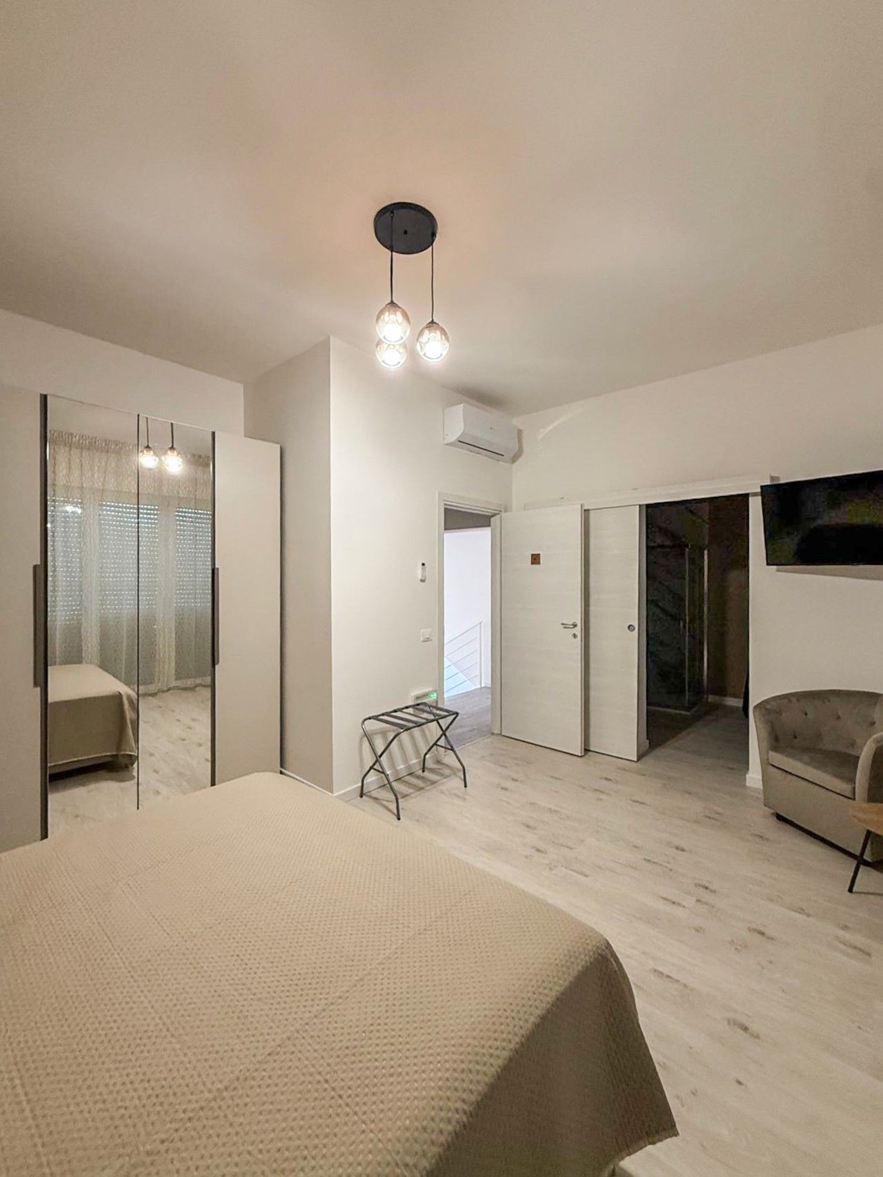 A hotel room with a bed, a chair, a small table, a TV, and a wardrobe.