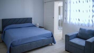 Een slaapkamer met een bed, een nachtkastje, een stoel en een deur naar een badkamer.
