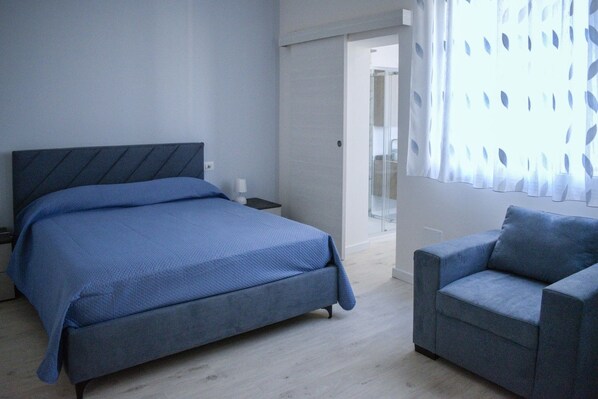Un dormitorio con una cama, una mesita de noche, una silla y una puerta que da al baño.