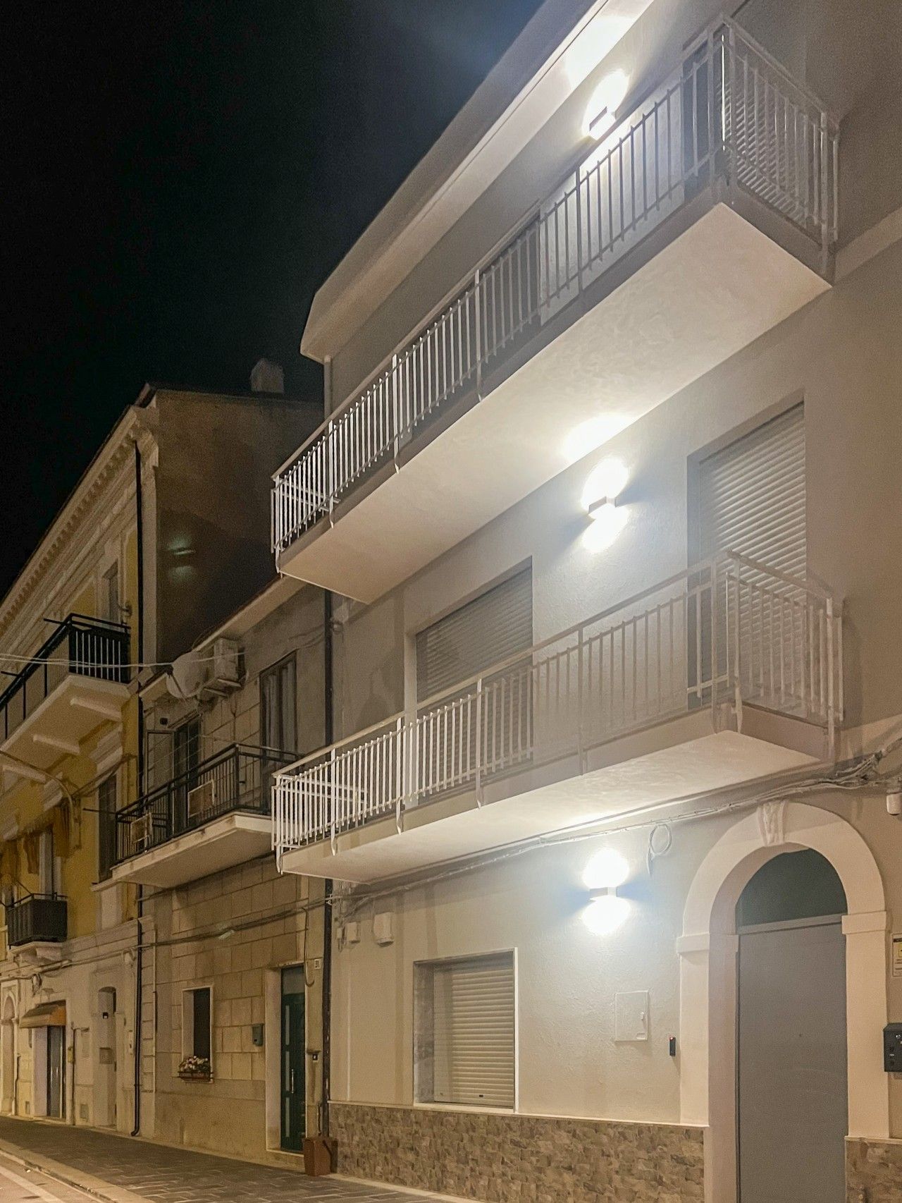 A multi-story building with balconies, a stone facade, and a door with a window.