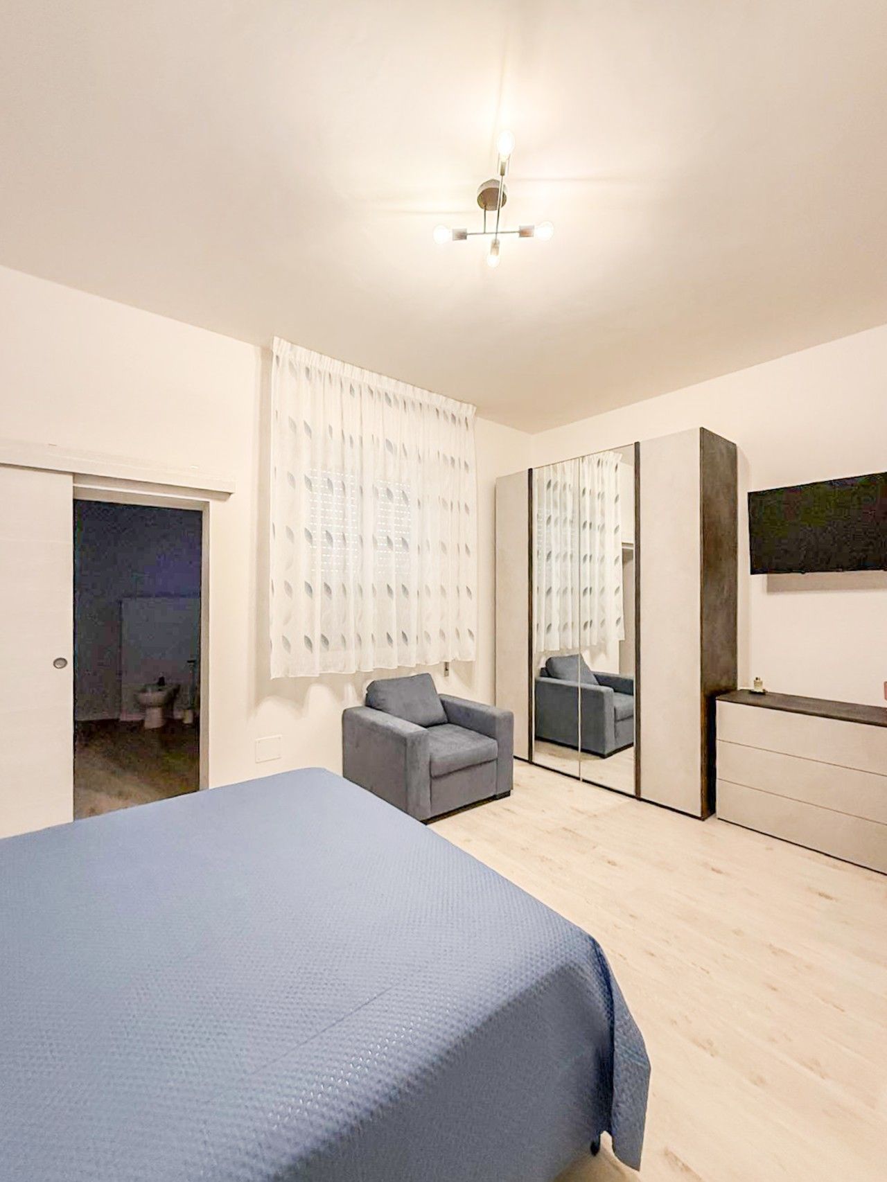 Un dormitorio con cama, una silla, cómoda y espejo.